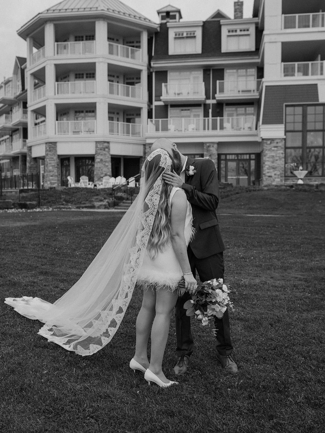 Black and white photo of bride Jillena in a modern mini dress with a cathedral-length 1970s French lace veil