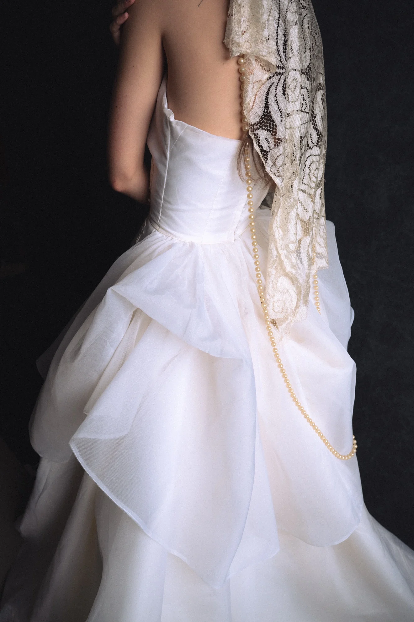 Back detail of a restored vintage gown with draped antique lace and a long strand of pearls