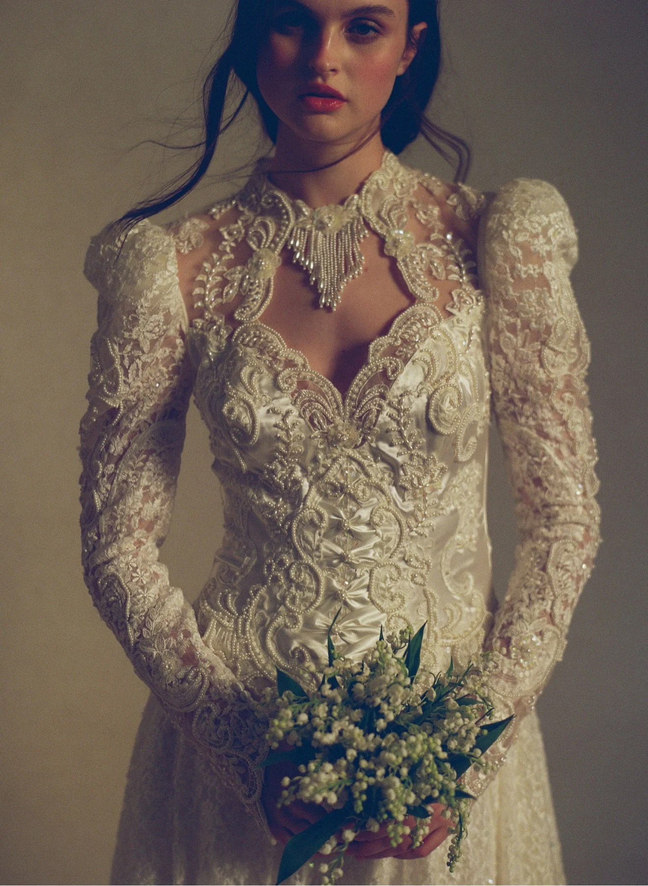 Close-up of an ornate beaded lace long-sleeve vintage gown, the bride holding a lily-of-the-valley bouquet